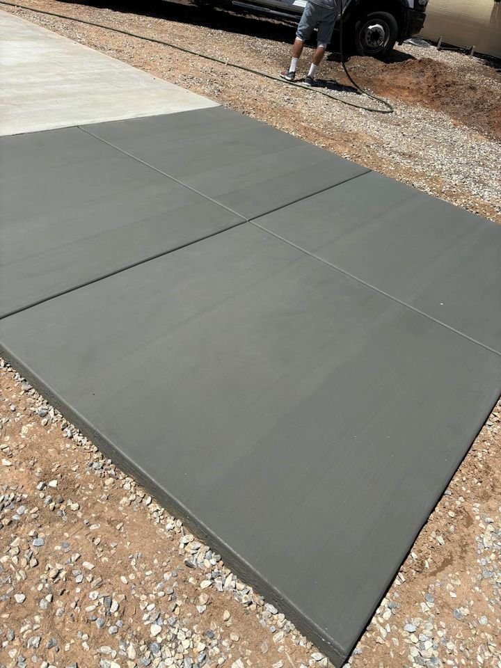 A freshly poured concrete driveway installation is sectioned into four parts, drying on the gravel and dirt surface in Mesa, AZ. In the background, a person is near a vehicle, likely involved in the construction process.