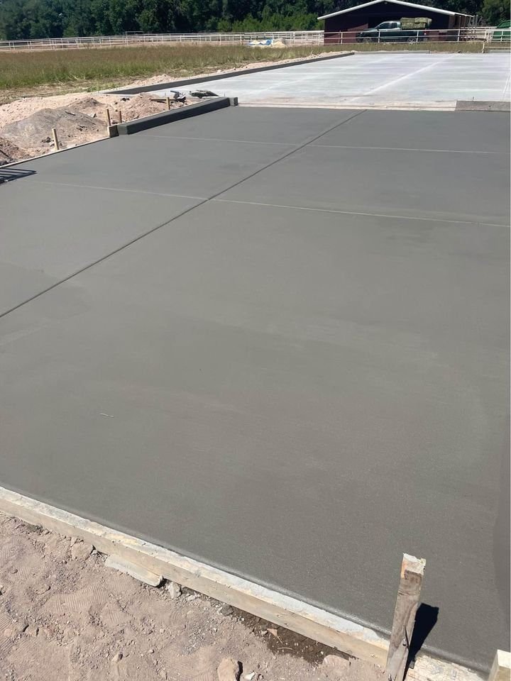 A freshly poured concrete slab by a renowned foundation contractor is seen at a construction site in Mesa, AZ. The smooth, gray surface is sectioned by control joints, with additional slabs and a partially visible structure in the background.