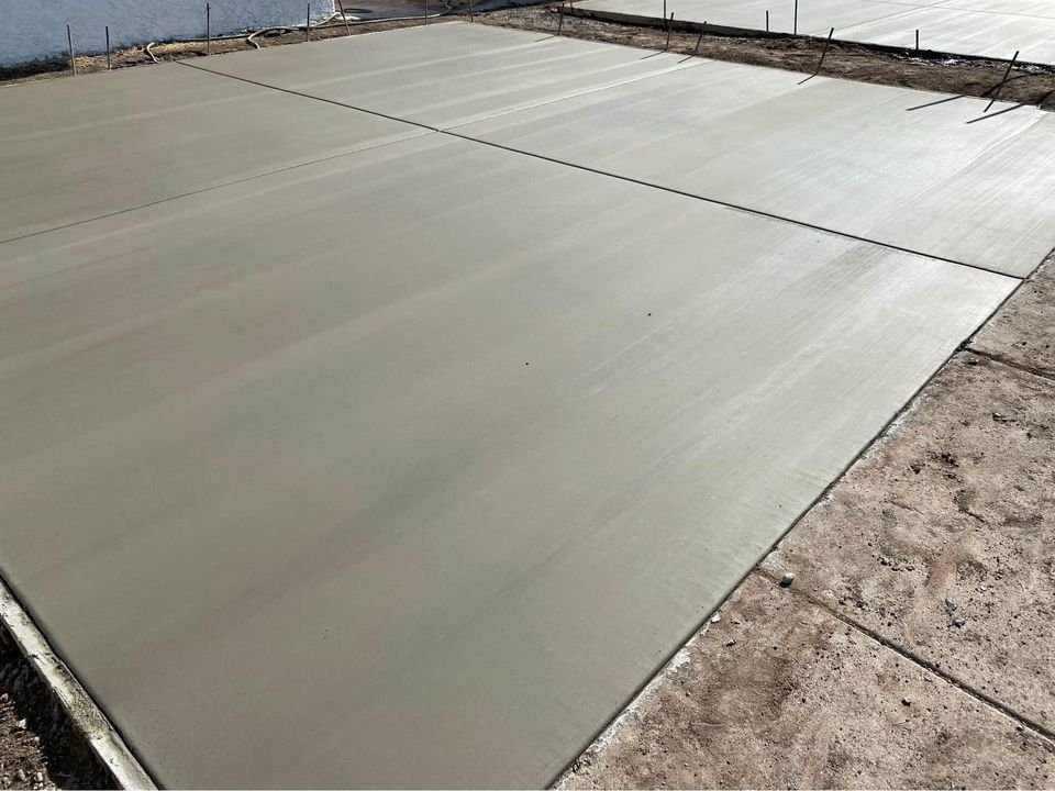 A freshly poured concrete slab, smooth and flat, covers the ground in a rectangular shape. Expertly laid by Mesa Master Concrete, it contrasts with the surrounding dirt surface. No additional structures or objects are visible in the immediate vicinity, showcasing their top-tier concrete services.