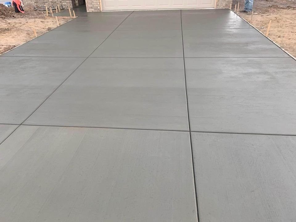 Freshly poured concrete driveway installation in Mesa, AZ, with visible division lines leading to a garage. The surrounding area is unfinished, and wooden stakes are visible on the sides, highlighting the ongoing concrete construction process.