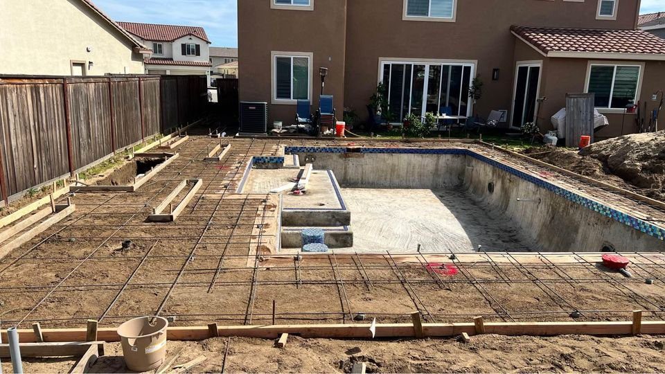 A backyard in the process of having an in-ground swimming pool constructed by skilled Arizona concrete contractors. The area is framed with wooden boards and rebar, indicating early stages of construction for this Scottsdale project. A two-story house looms elegantly in the background.